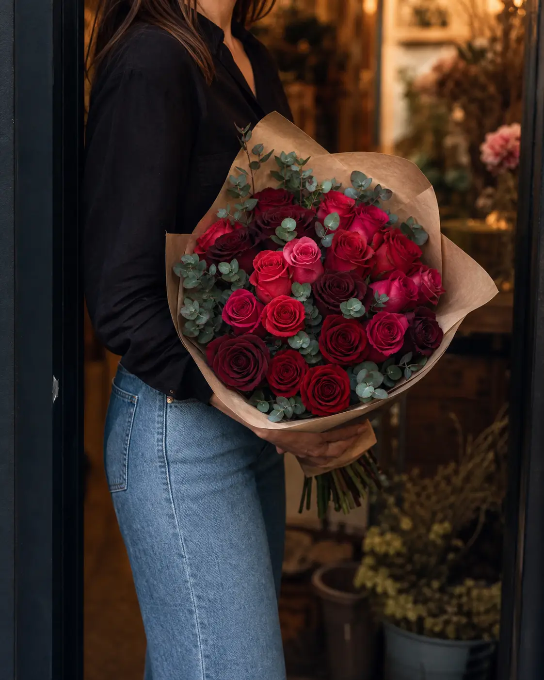 A hand-tied bouquet of red and pink roses being carried from a flower studio