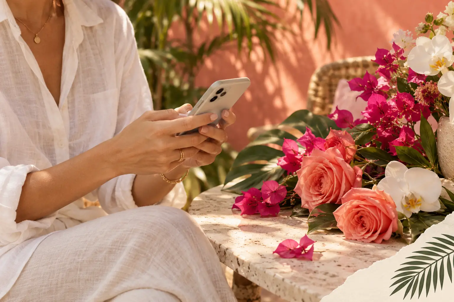 Hands holding a phone beside coral roses and white orchids on a sunlit tropical patio